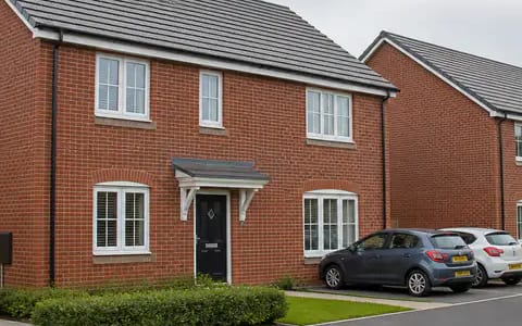 Red brick house with a grey porch, white windows and black front door on a new estate